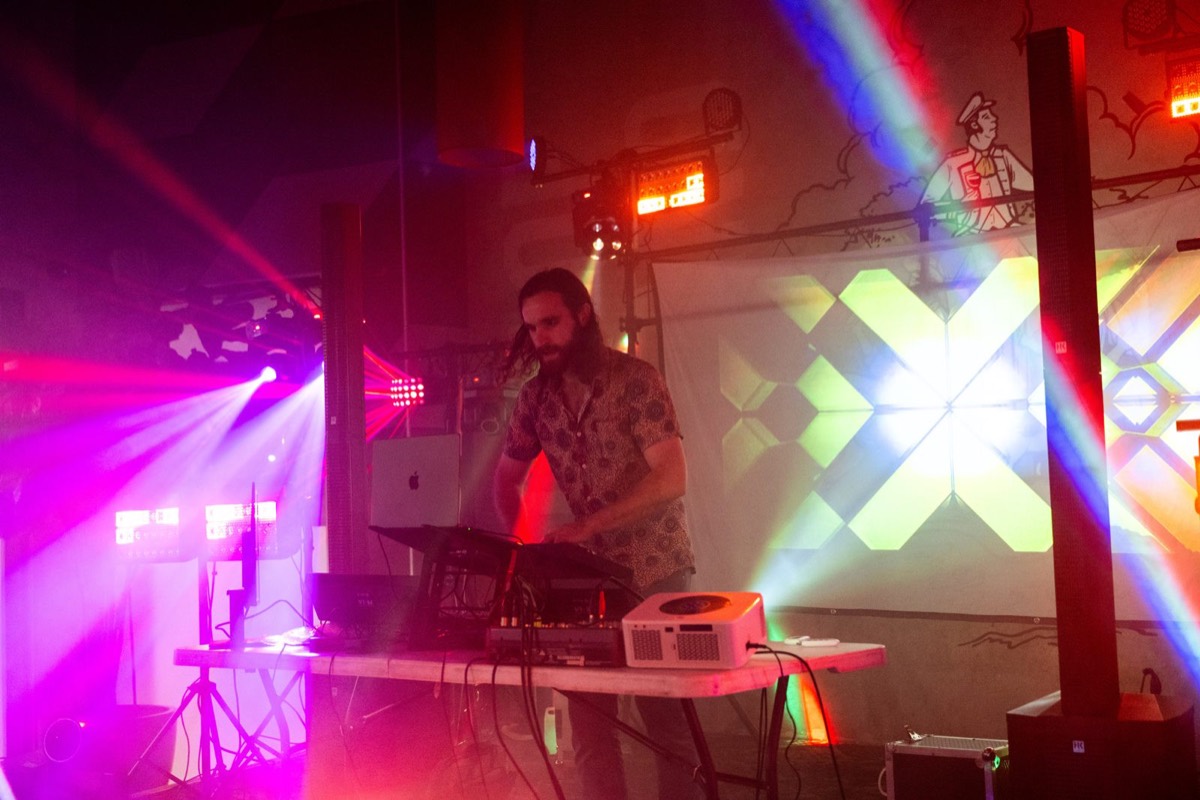 DJ performing at the decks with light beams across the stage