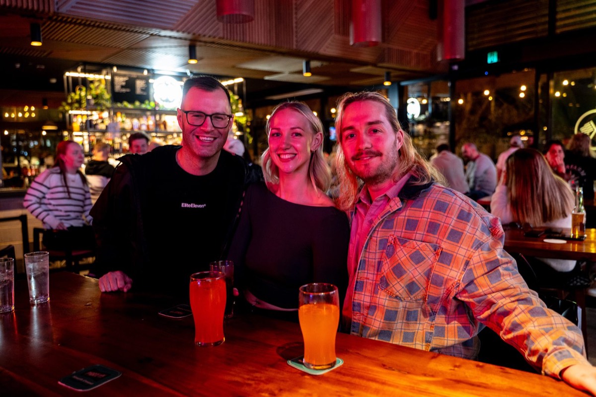 Three friends smiling with beers at the bar